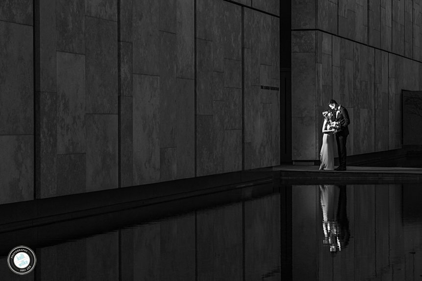photo of bride and groom standing together with their reflection in front of them off a pool of water in philadelphia 