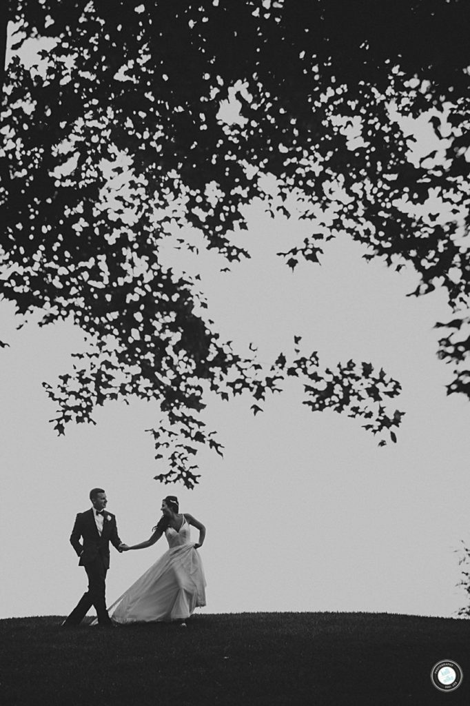 black and white photo of bride leading groom across a hillside at penn oaks golf club in west chester pa