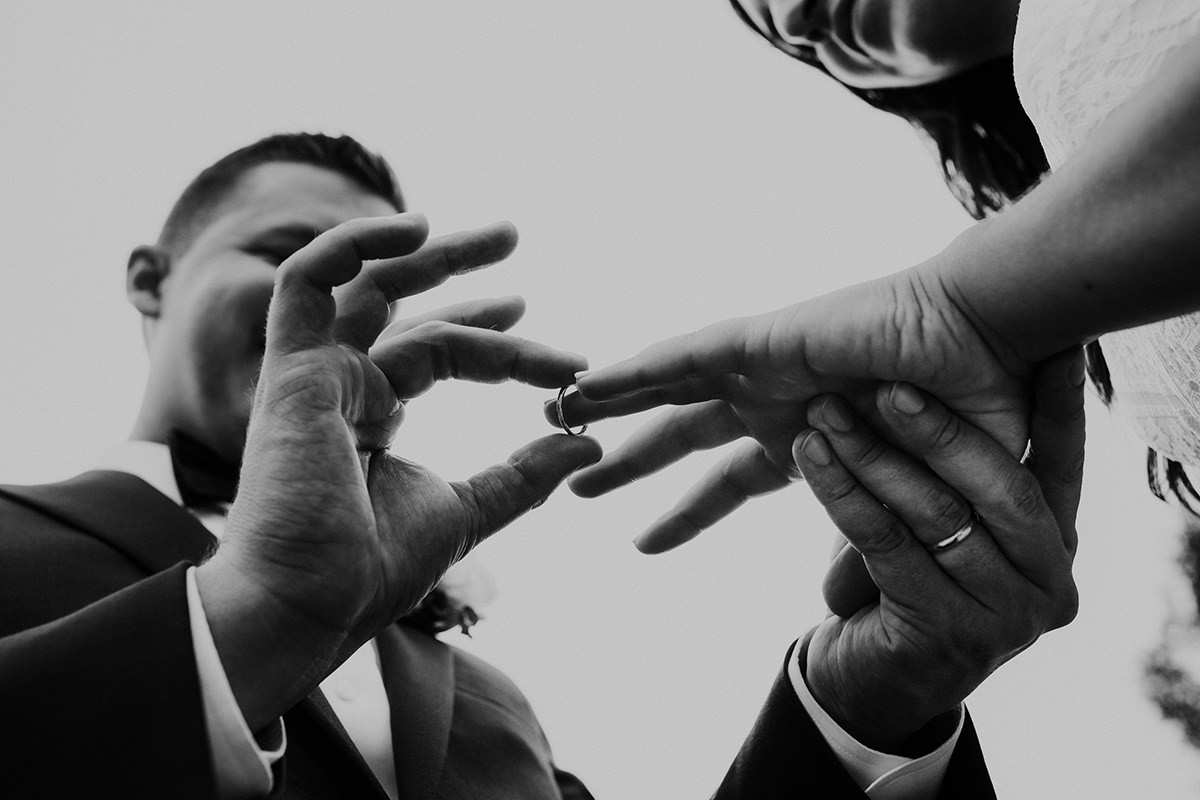 black and white photo of a groom putting the wedding ring on bride's hand