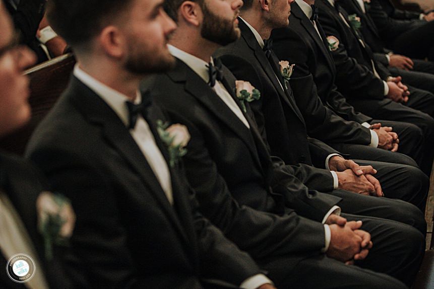 detail of the groomsmens hands clasped in their laps while sitting at a catholic wedding in wilmington delaware