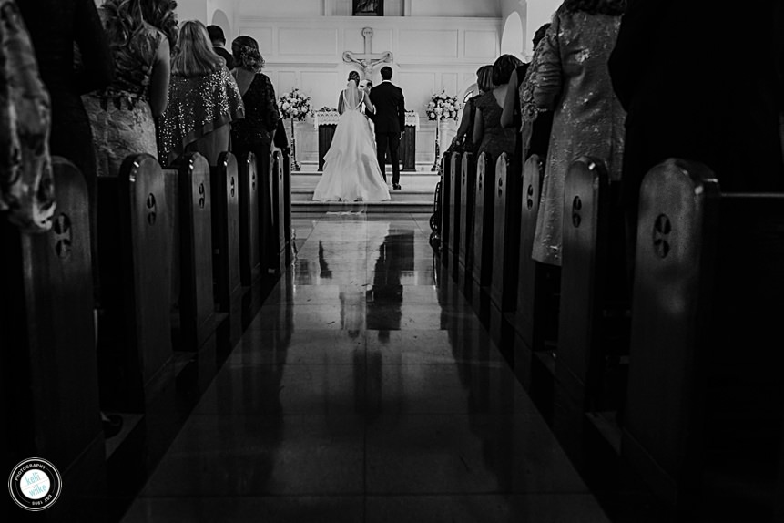 bride and grooms backs with reflection on floor looking up the aisle at a church wedding ceremony at st. josephs on the brandywine in wilmington delaware