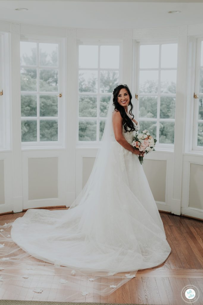 Bride poses at Greenville Country Club in Greenville DE with her peony bouquet with peach and pink and white . She wears a Lazaro wedding gown