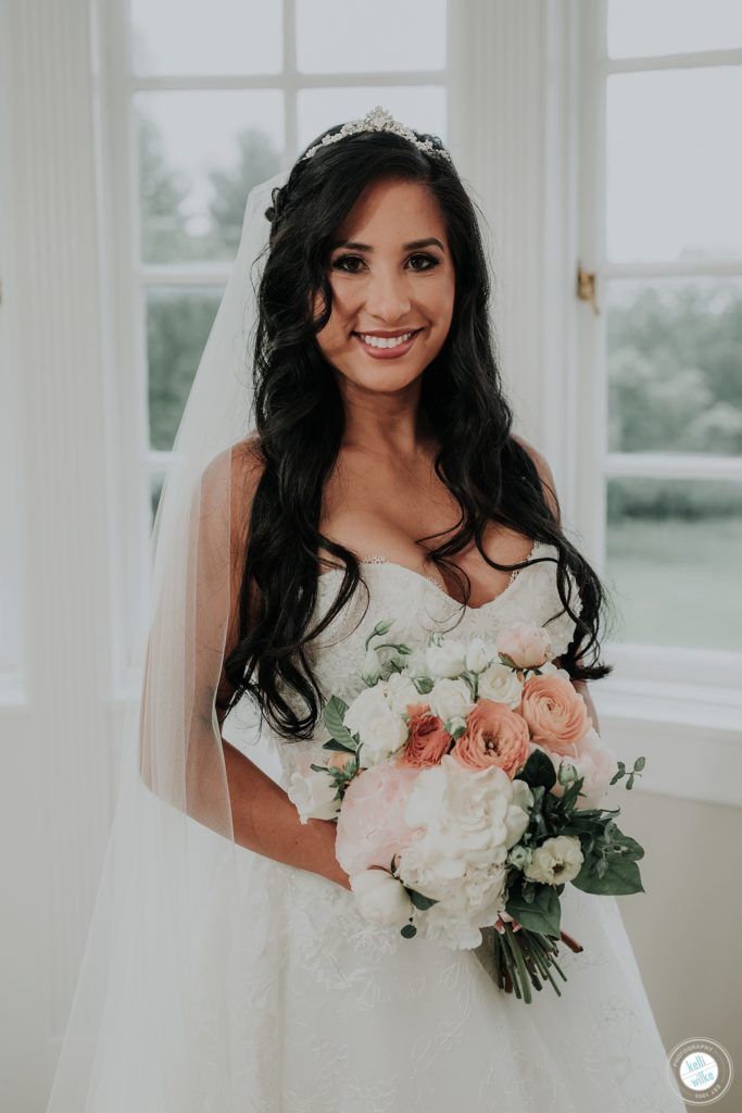 Bride poses at Greenville Country Club in Greenville DE with her peony bouquet with peach and pink and white . She wears a Lazaro wedding gown
