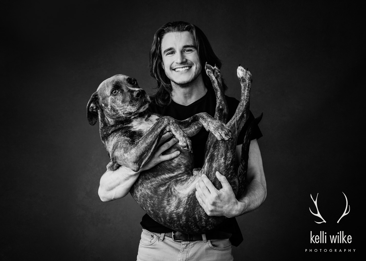 A picture of a young man holding a large dog in his arms like a baby, photographed by Kelli Wilke Photography in Wilmington, DE. 