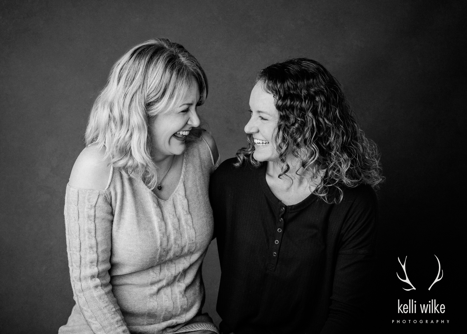 A photo of a mom and her adult daughter sharing an embrace and smiling at each other, photographed by Kelli Wilke Photography in Wilmington, DE. 
