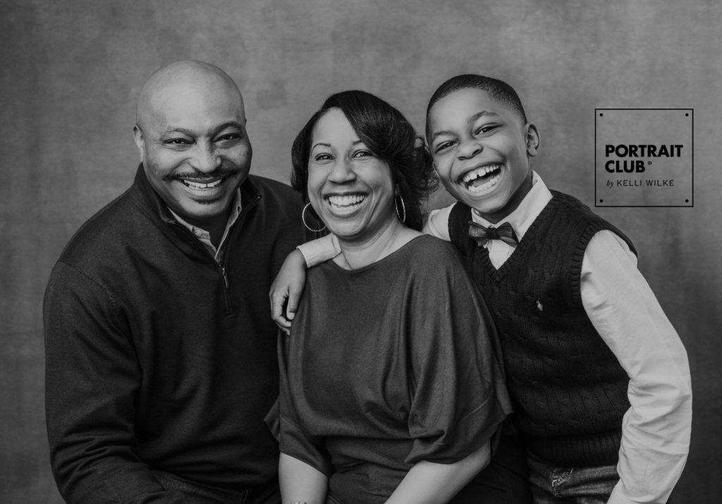 A candid portrait of a family smiling at the camera during their family portrait session with Portrait Club by Kelli Wilke. 