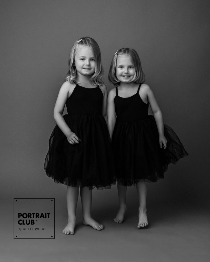 A formal portrait of two little girls in black tutus smiling at the camera during a photo session with Kelli Wilke Photography. 