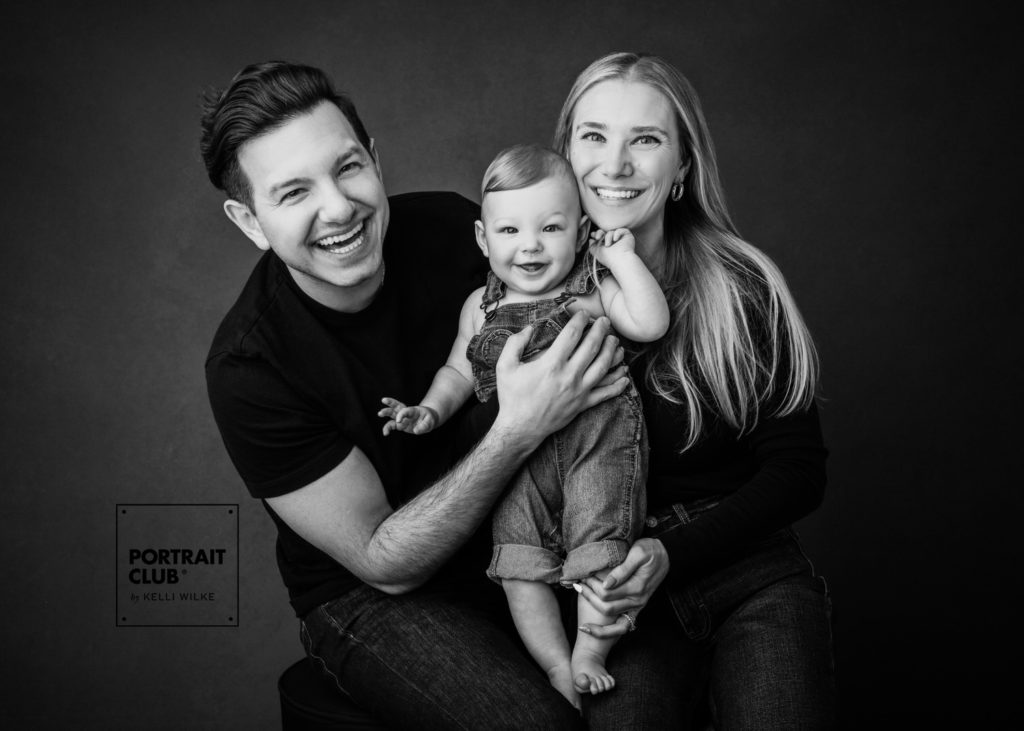 A candid picture of a family smiling at the camera during a family photo session with Portrait Club by Kelli Wilke. 