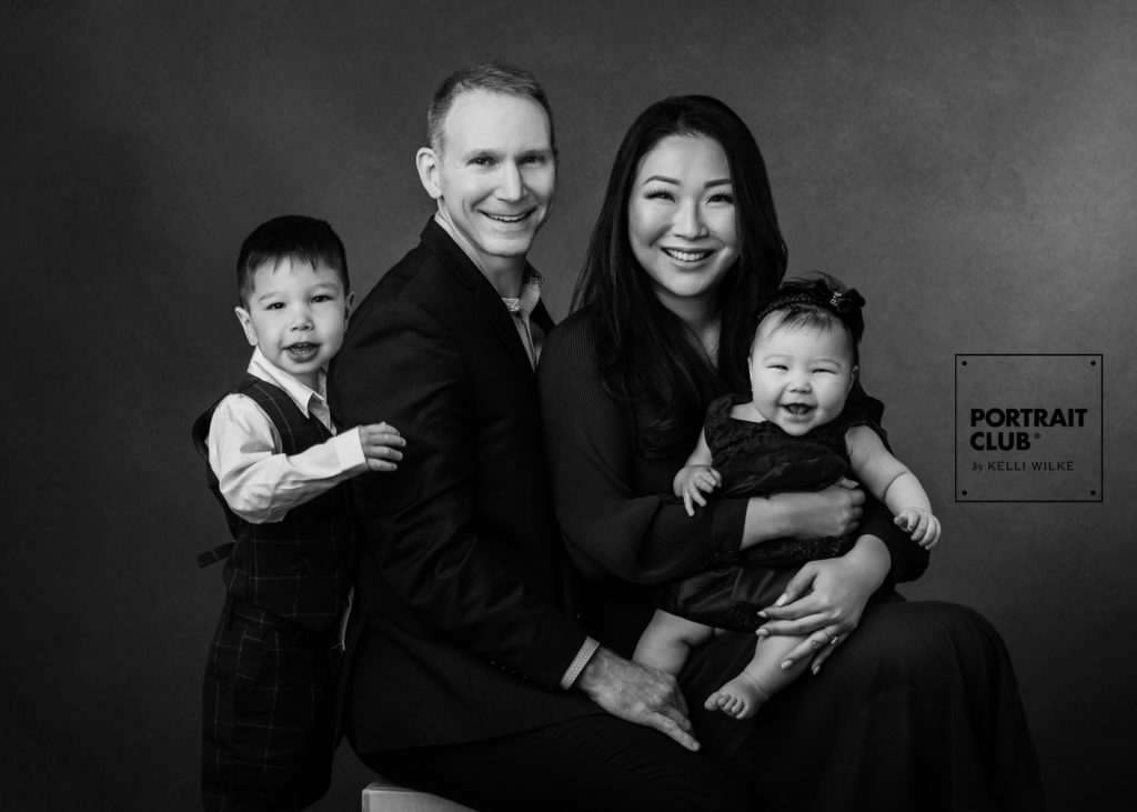 A formal portrait of a family with two young children smiling at the camera during a family photo session with Portrait Club by Kelli Wilke. 